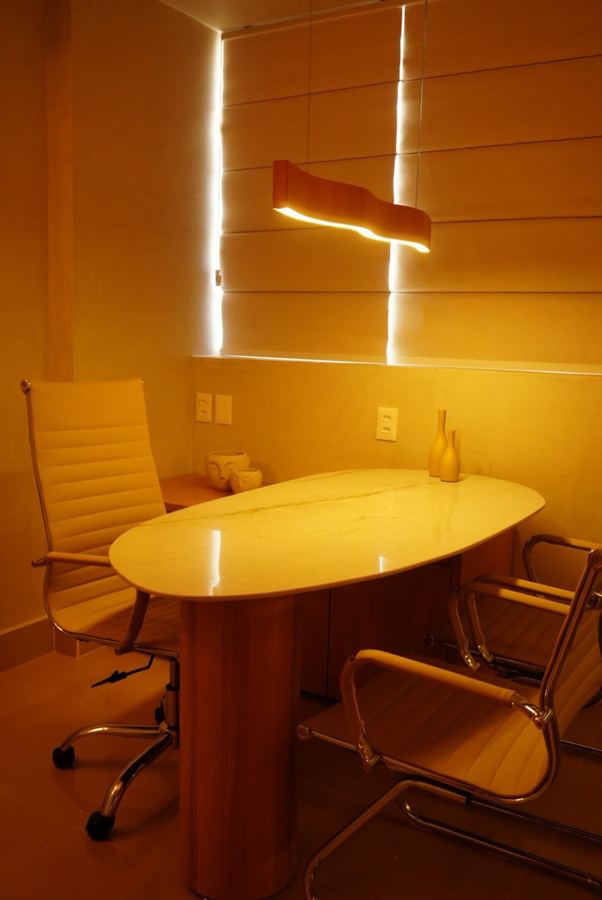 Consultório à noite, com luz quente no pendente ondulado e mesa oval